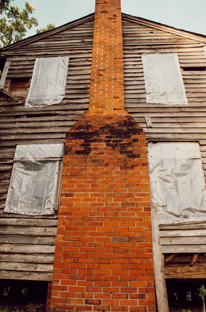 1800's farmhouse with wood siding and red brick chimney turned into a construction horror story