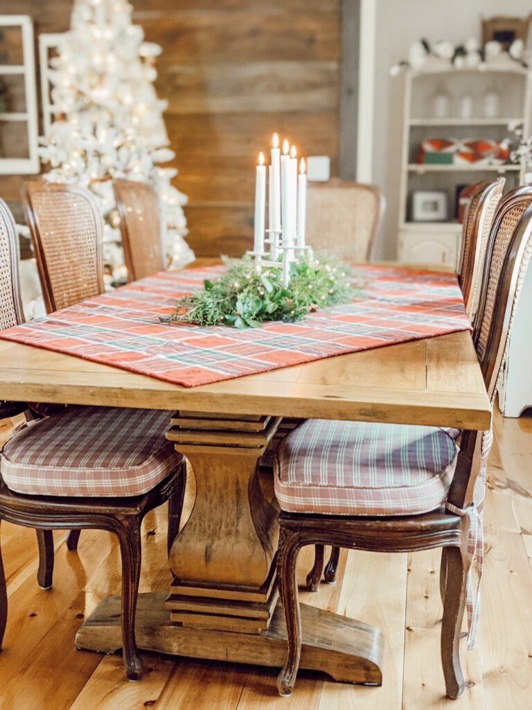 trestle table decorated for Christmas with red plaid tablecloth, greenery and candles